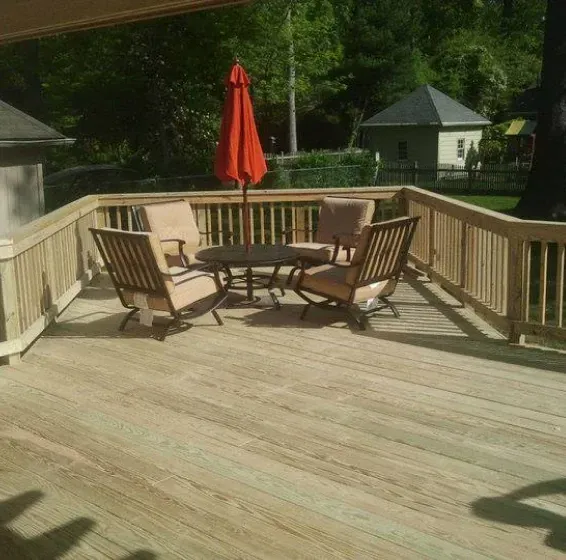 Wooden deck with outdoor furniture and orange umbrella, overlooking a yard.