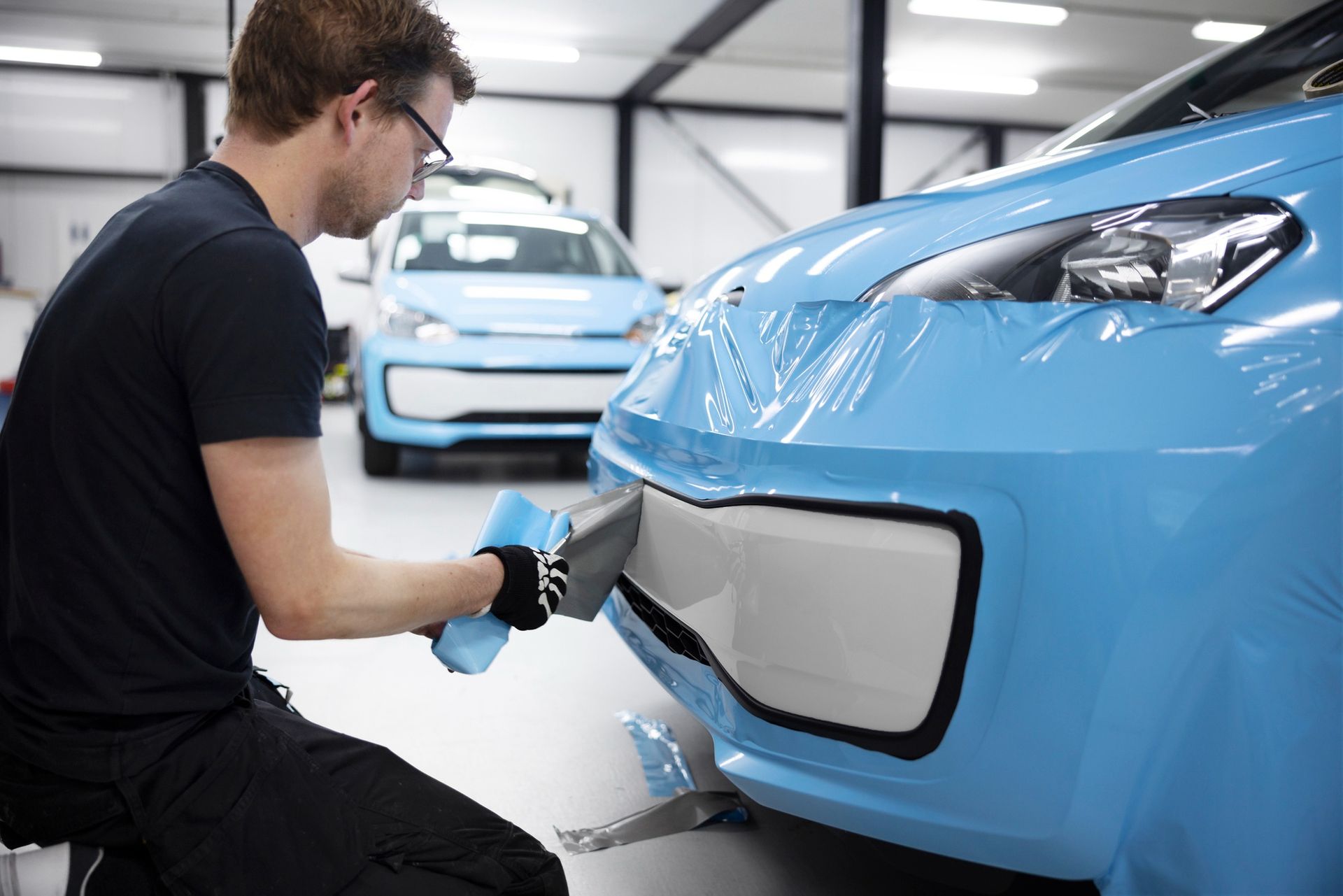 A person wearing black gloves is cleaning a black car with a blue cloth.