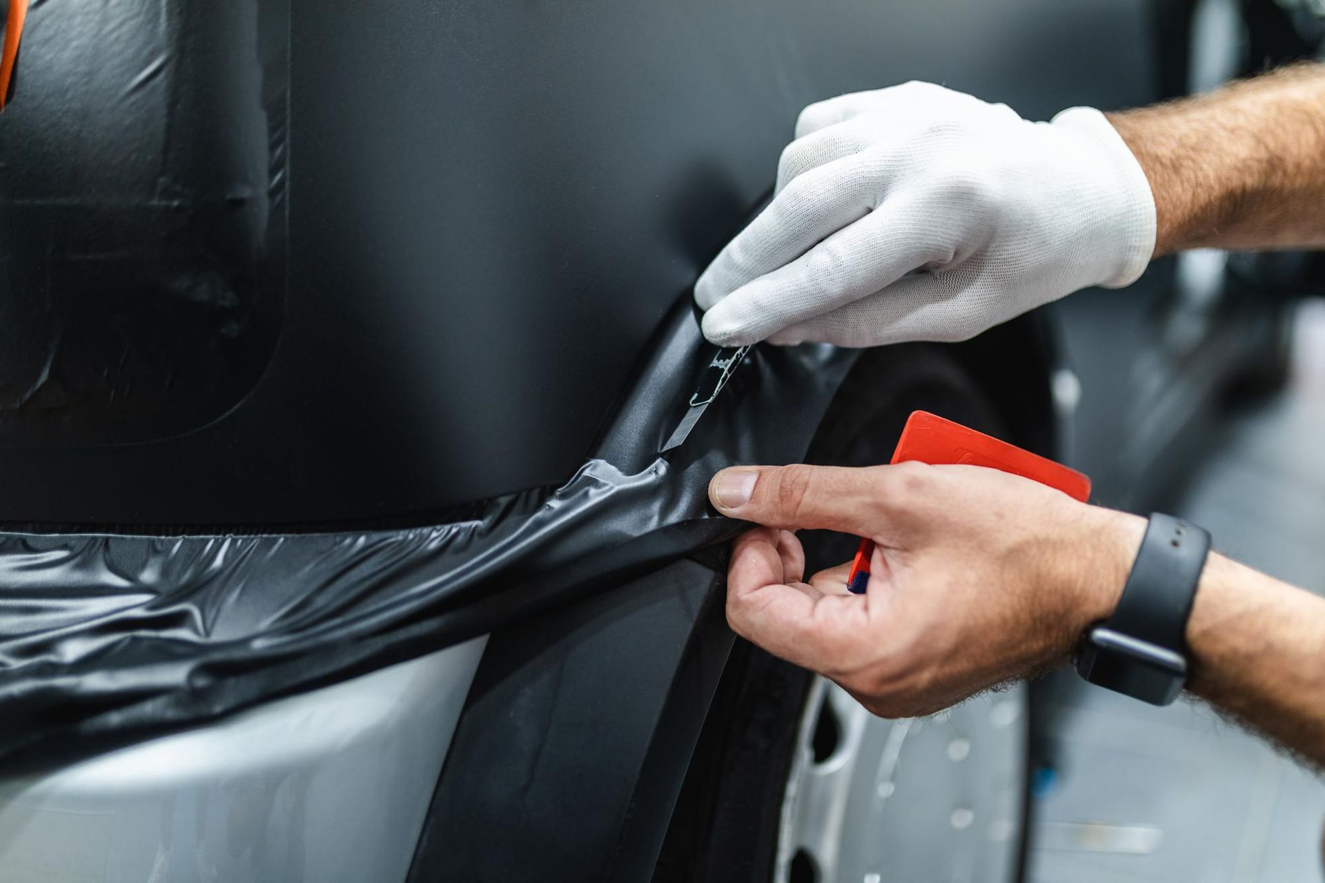 A man is wrapping a car in black vinyl wrap.