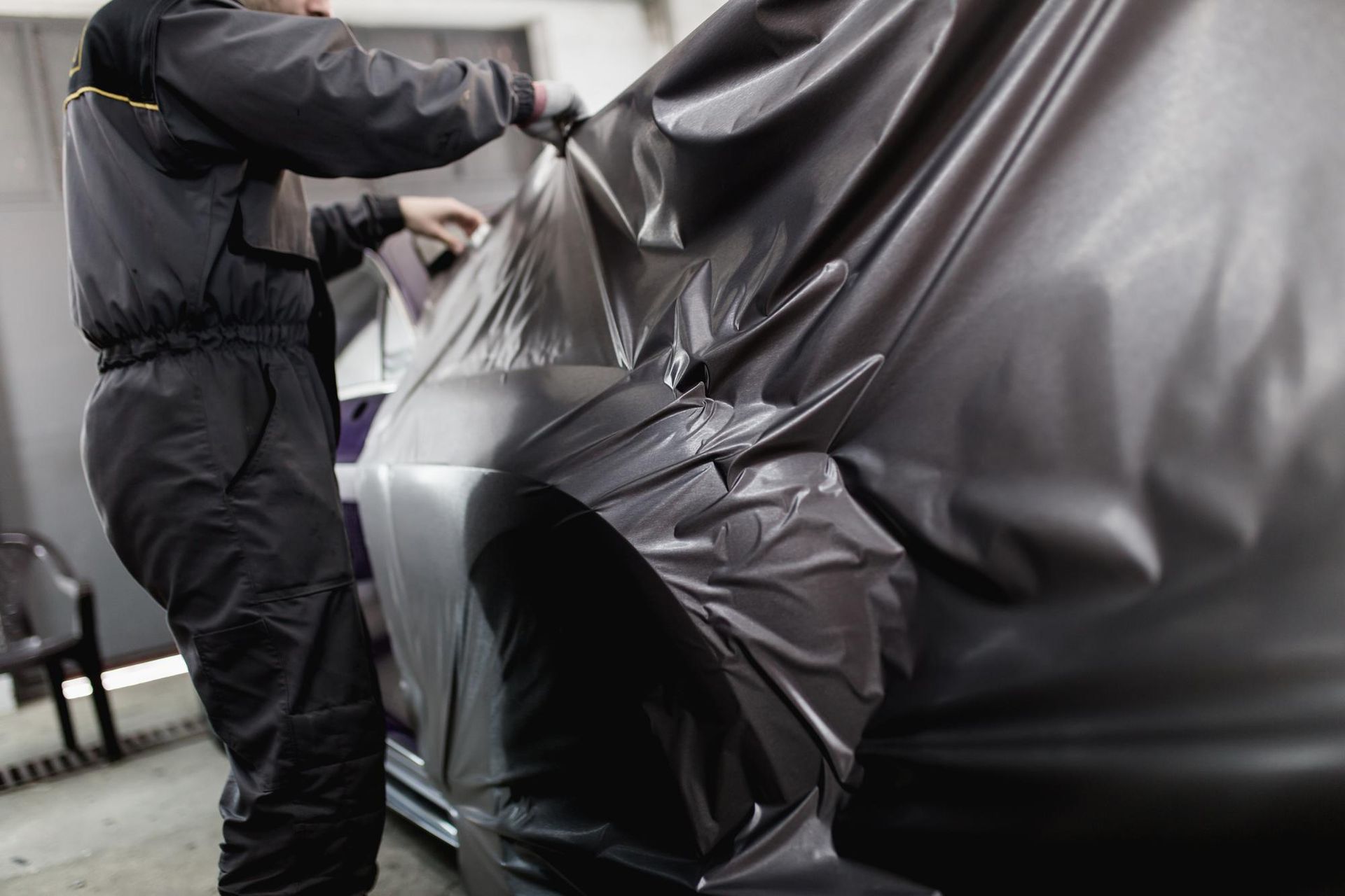 A man is wrapping a car in black vinyl.