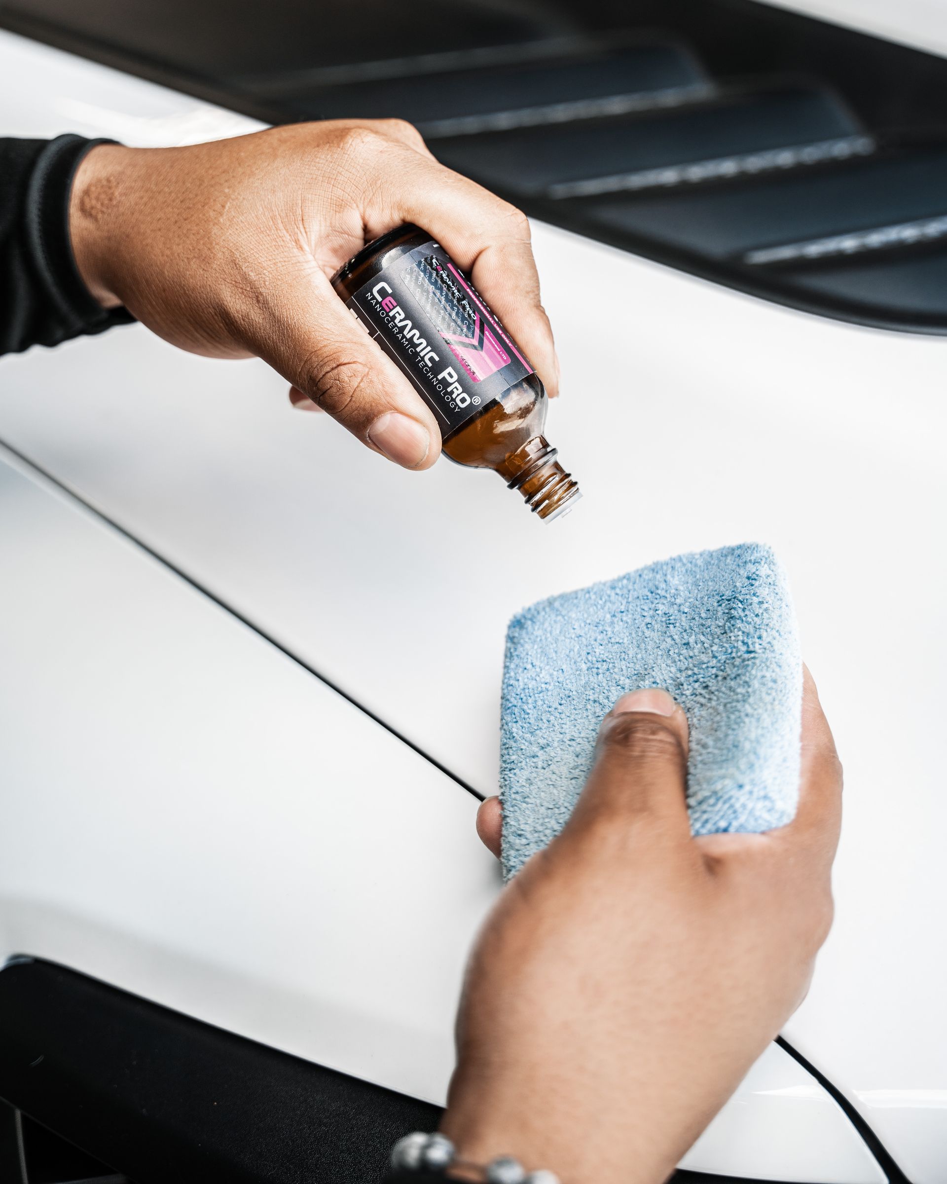 A person is applying a ceramic coating to a white car.