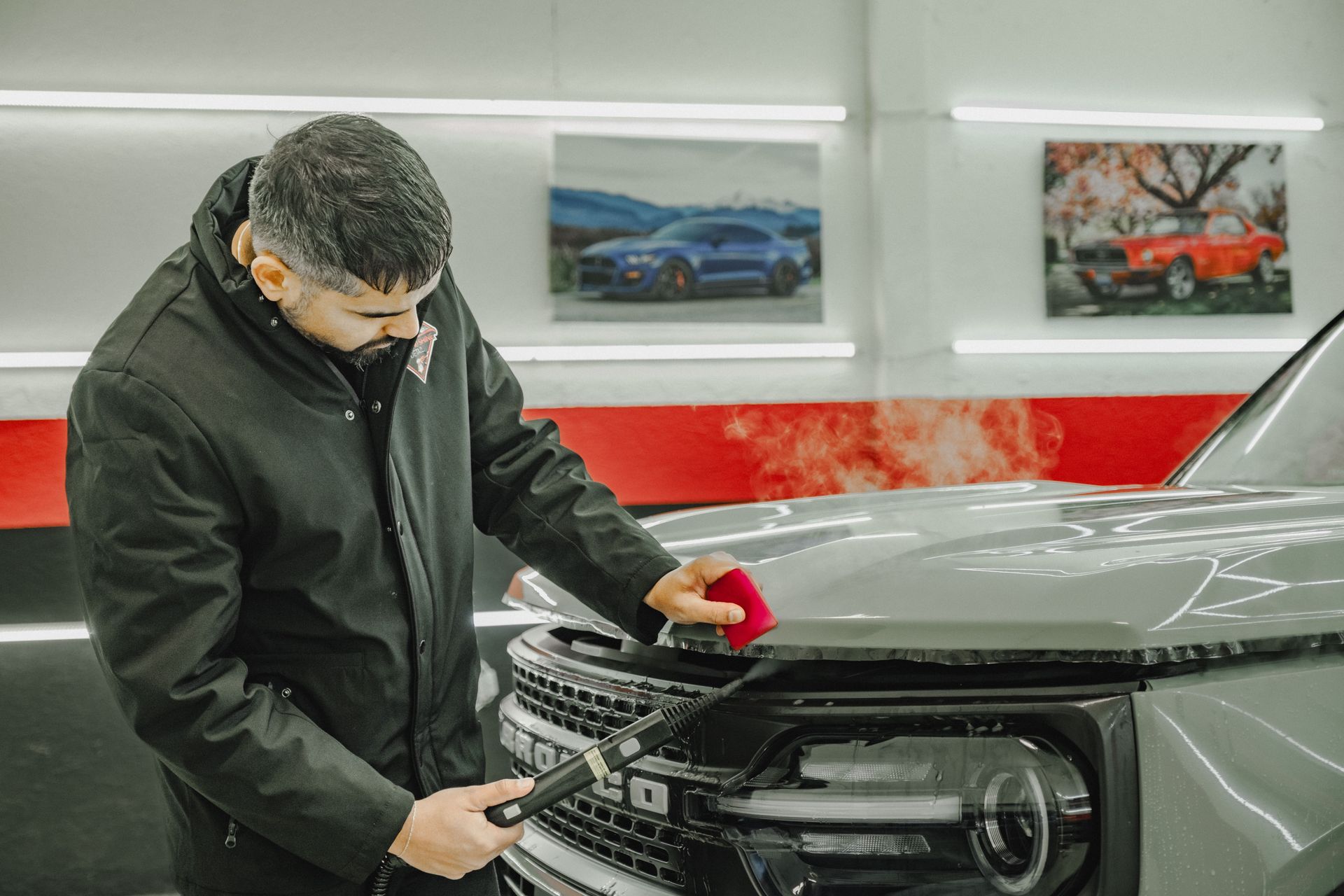 A man is cleaning the hood of a car in a garage.