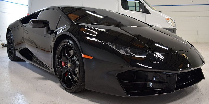 A black lamborghini huracan is parked in a garage next to a white van.