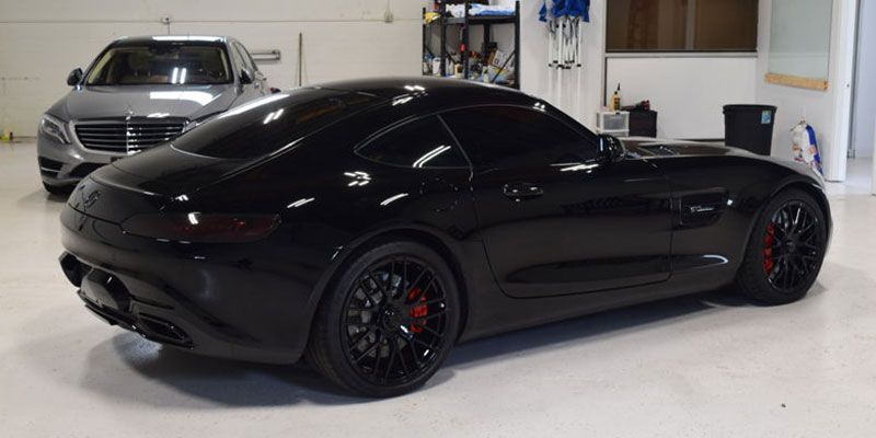 A black sports car is parked in a garage next to a silver car.