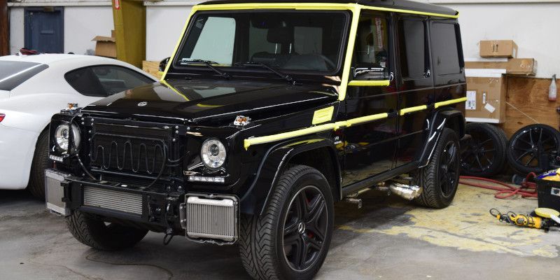 A black mercedes benz g63 is parked in a garage next to a white car.