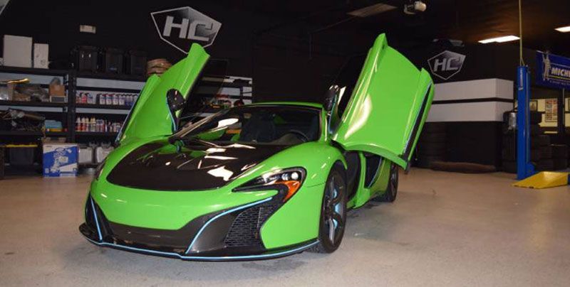 A green sports car is parked in a garage with its doors open.