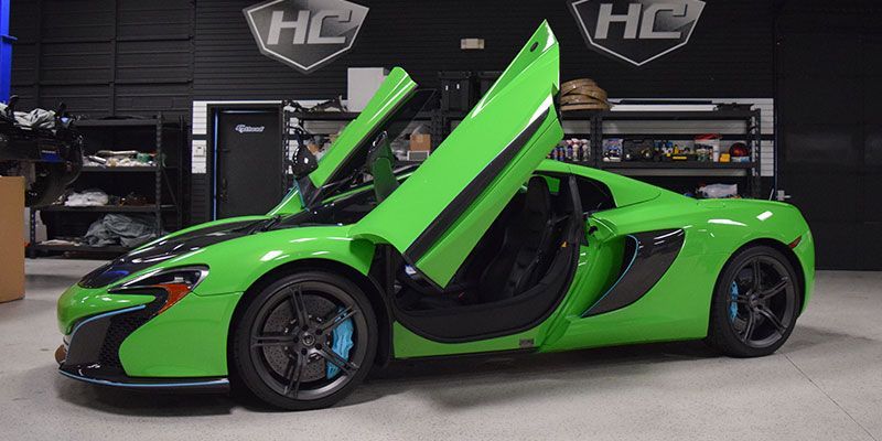 A green sports car with its doors open is parked in a garage.