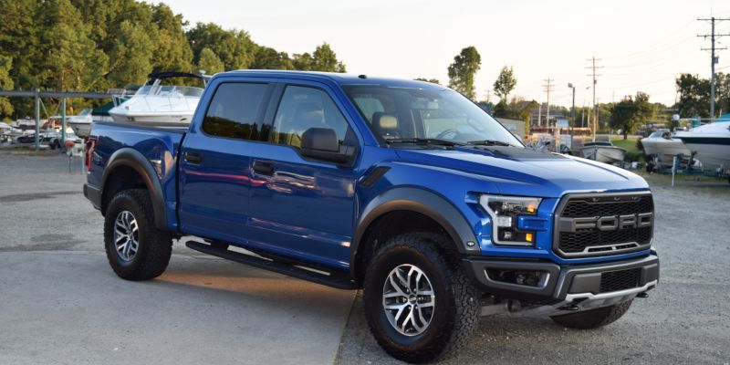 A blue ford raptor truck is parked in a parking lot next to a boat.