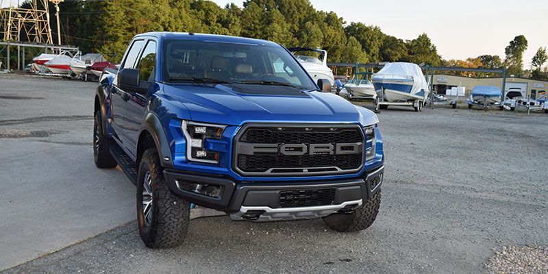 A blue ford raptor truck is parked in a parking lot.