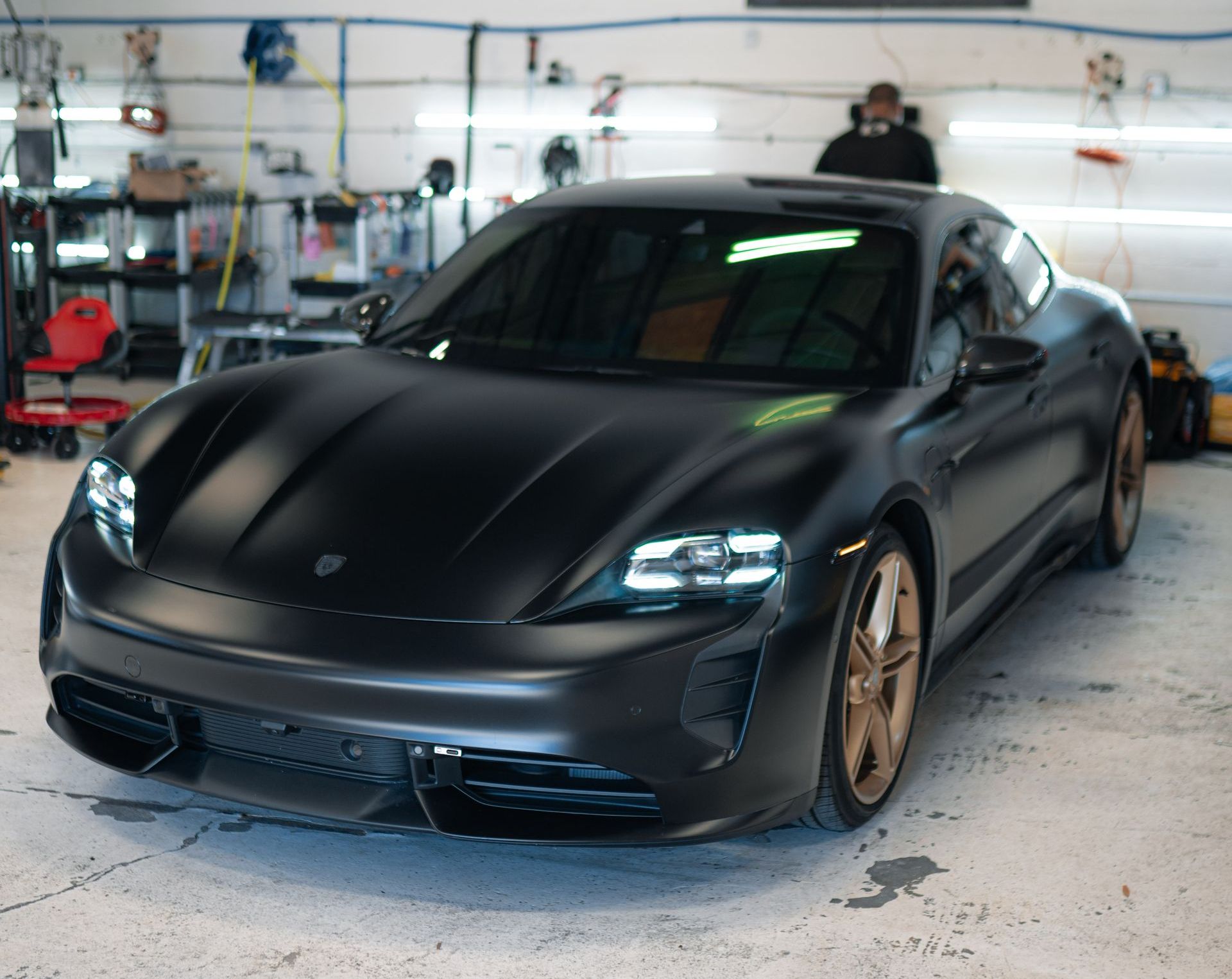 A person wearing black gloves is cleaning a black car with a blue cloth.