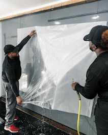 Two men are cleaning a glass wall with a hose.