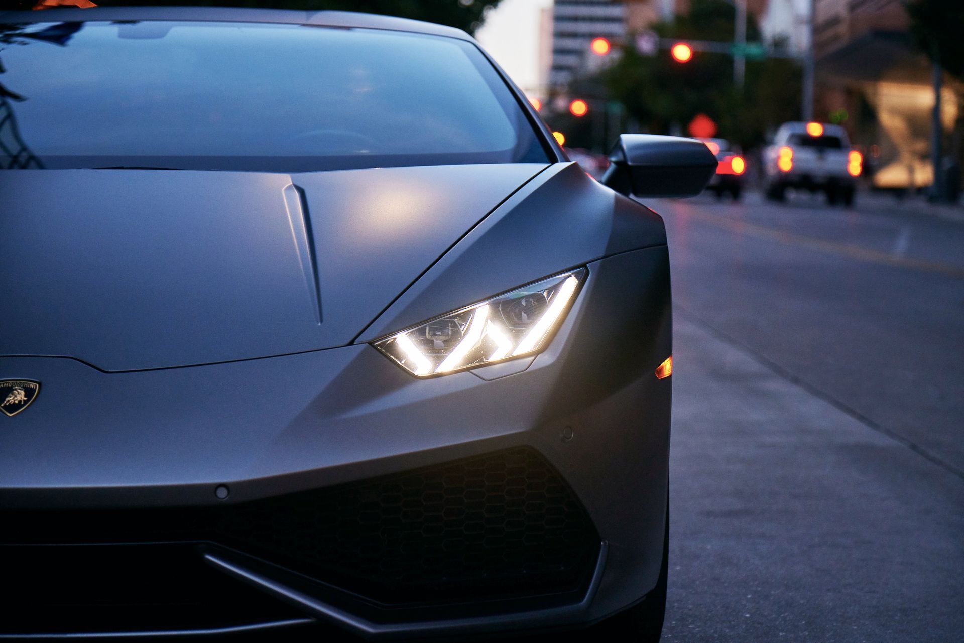 Close-up of a gray sports car with headlights on, parked on a city street at dusk