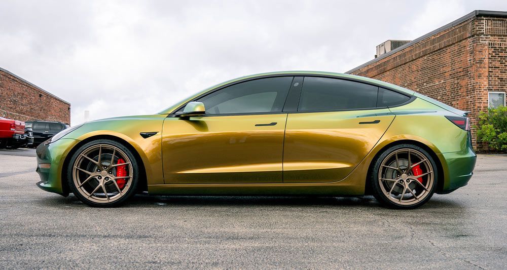 A tesla model 3 is parked in a parking lot in front of a building.