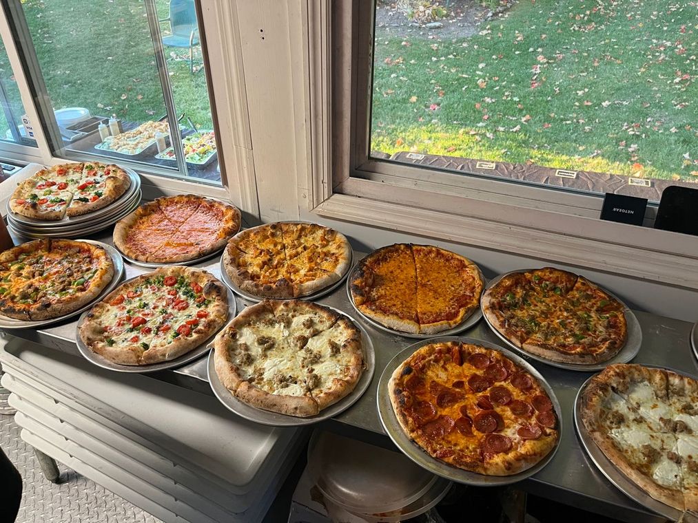 A variety of pizzas are sitting on a table in front of a window.