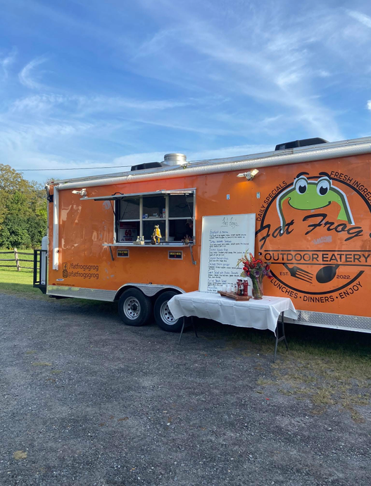 A food truck with a frog on the side is parked in a parking lot.