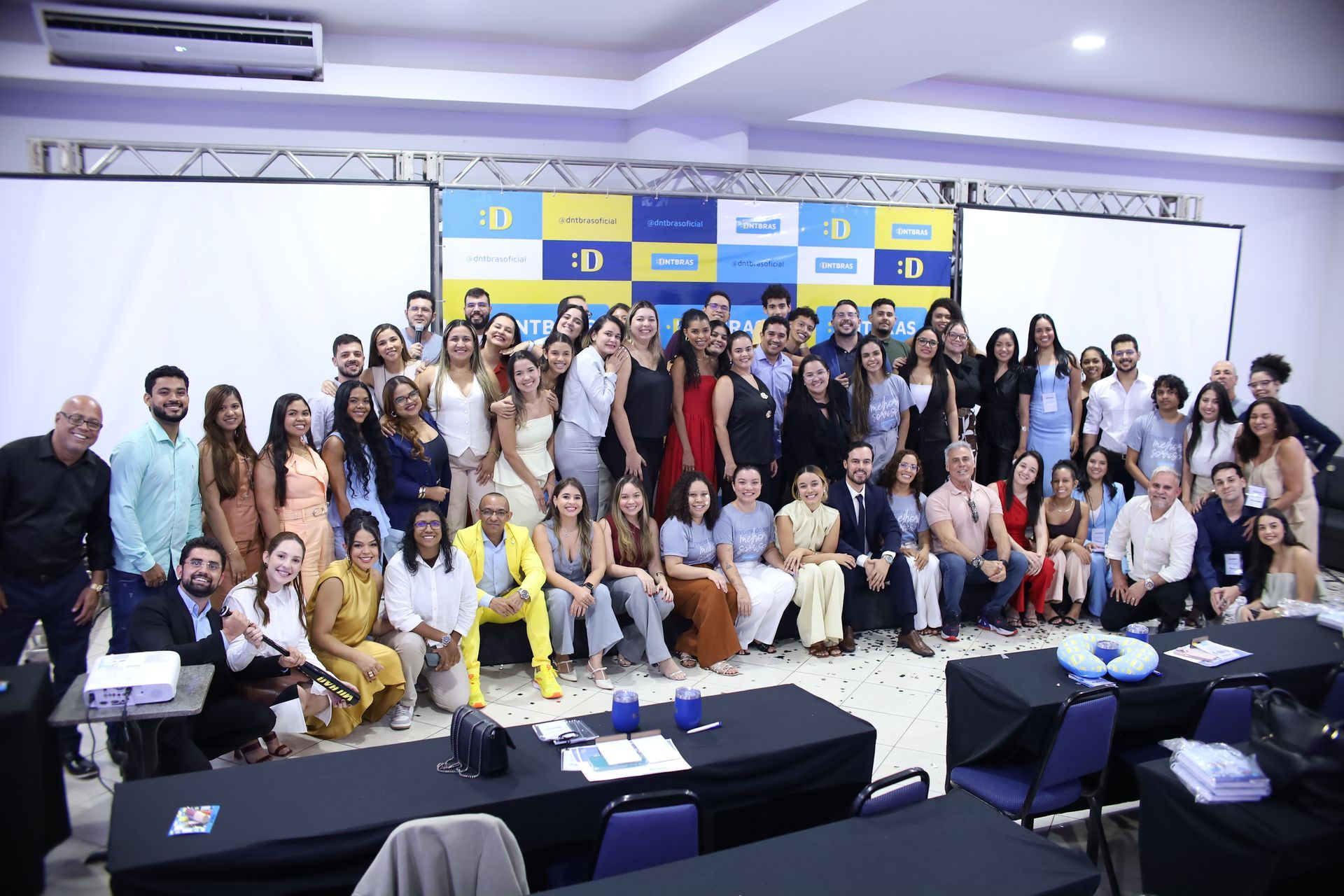 Foto de grupo de várias pessoas em uma sala de conferências com um logotipo ao fundo.