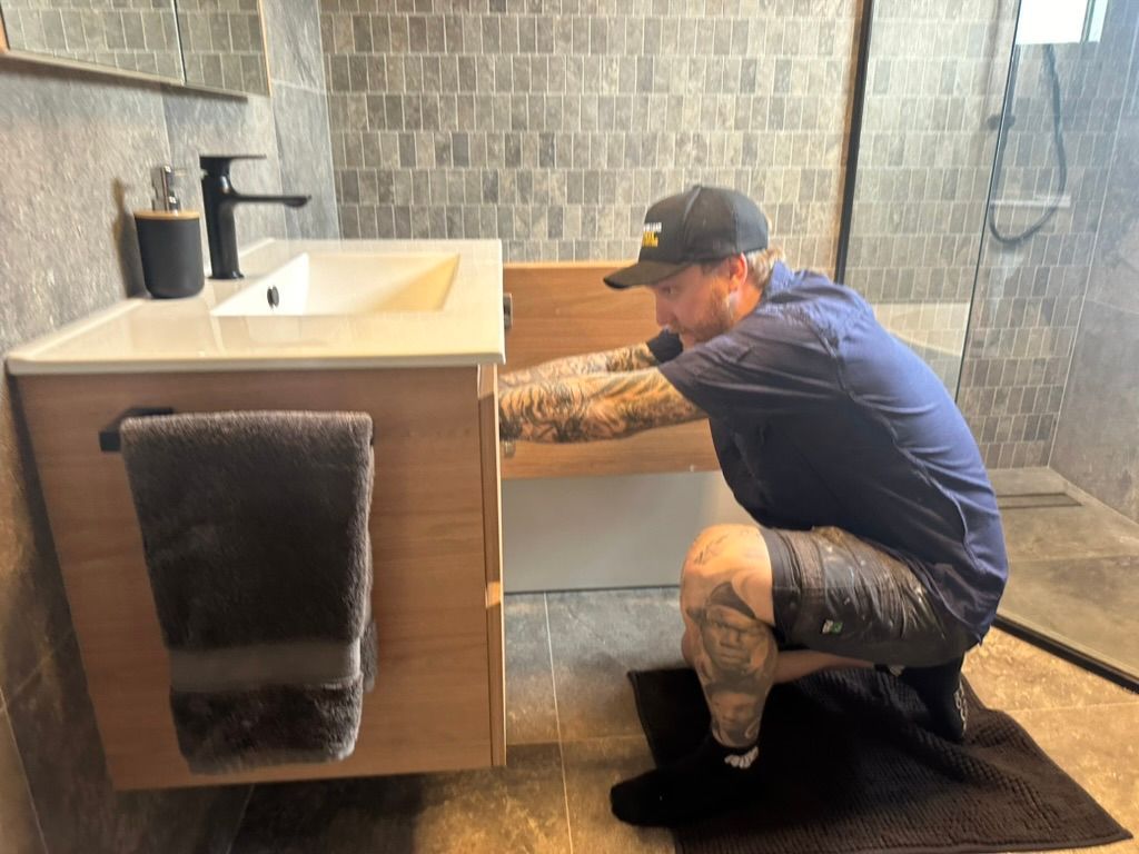 Man Installing a Bathroom Vanity, Crouching Near Open Cabinet — Hot Water Specialist Forster In Forster, NSW