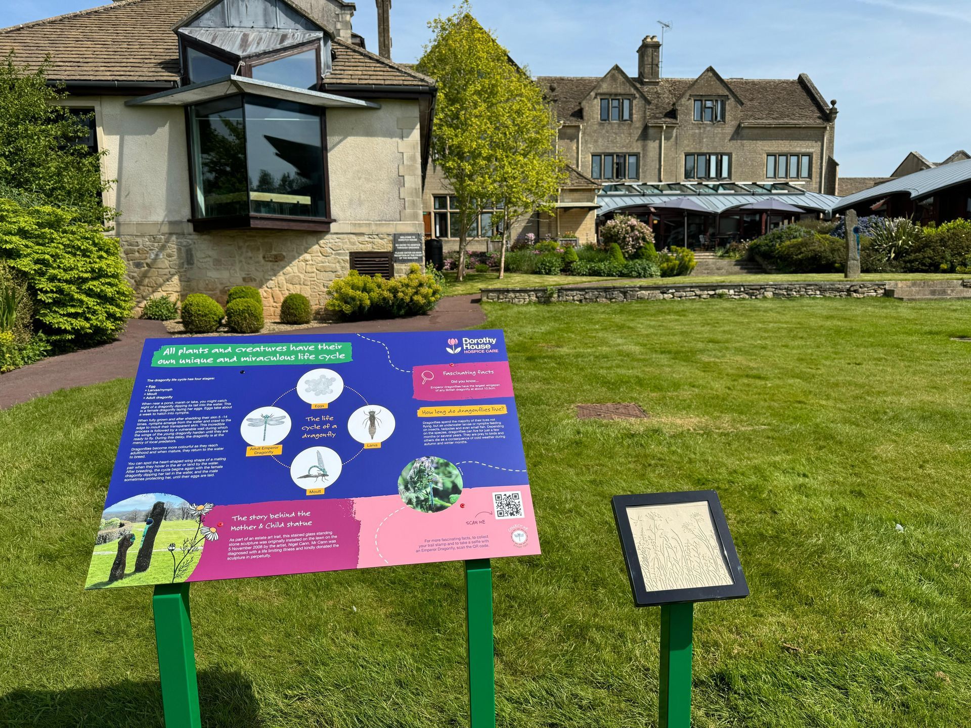 A sign in a park with a house in the background