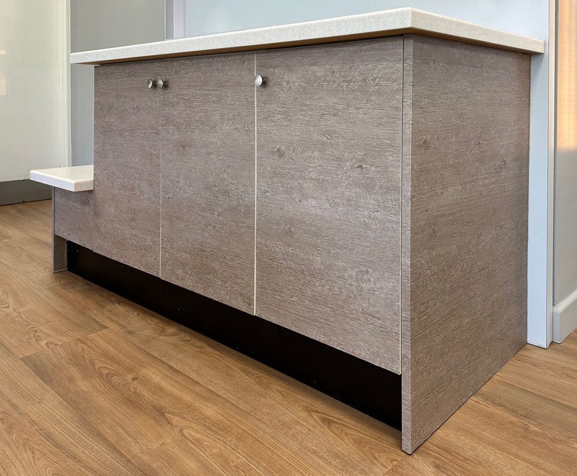 A wooden cabinet with a white counter top is sitting on a wooden floor.