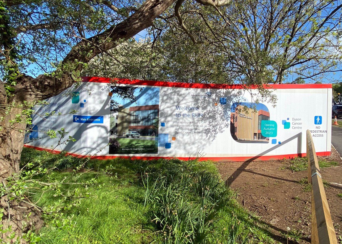 A large white and red sign is sitting in the grass next to a tree.