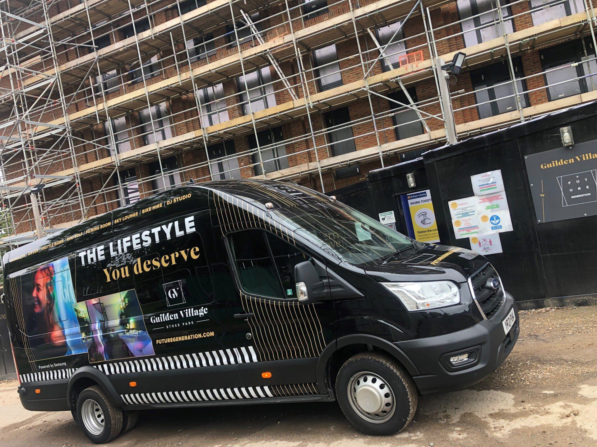 A black van is parked in front of a building under construction.