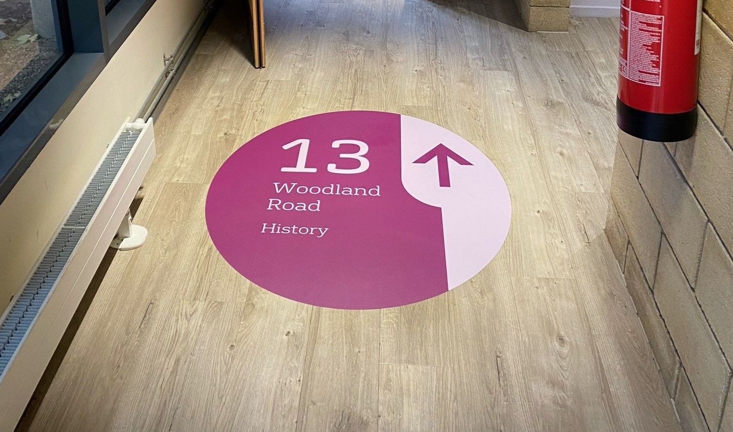 A pink and white circle with the number 13 on it is on the floor of a hallway.