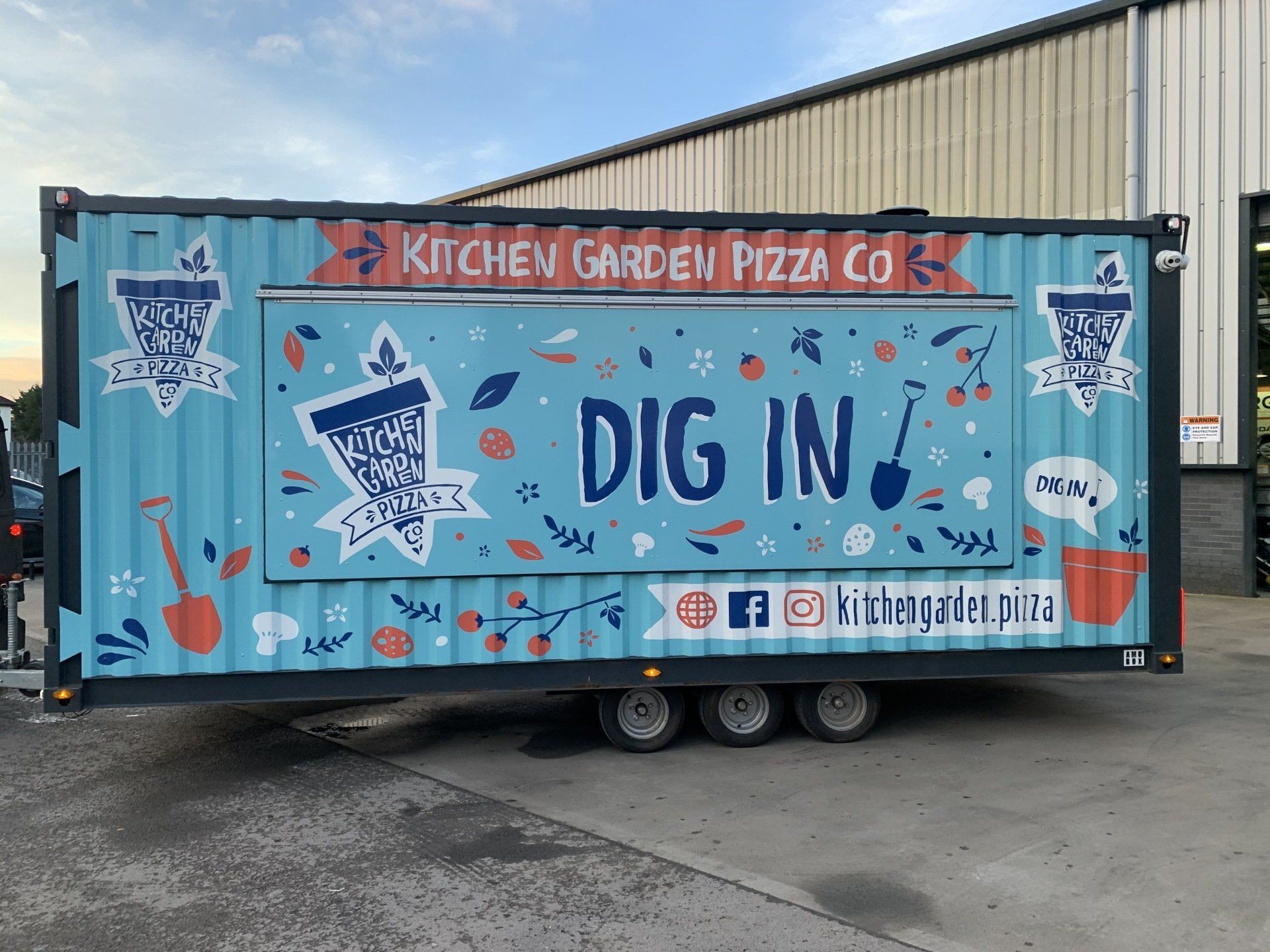 A kitchen garden pizza co trailer is parked in front of a building.