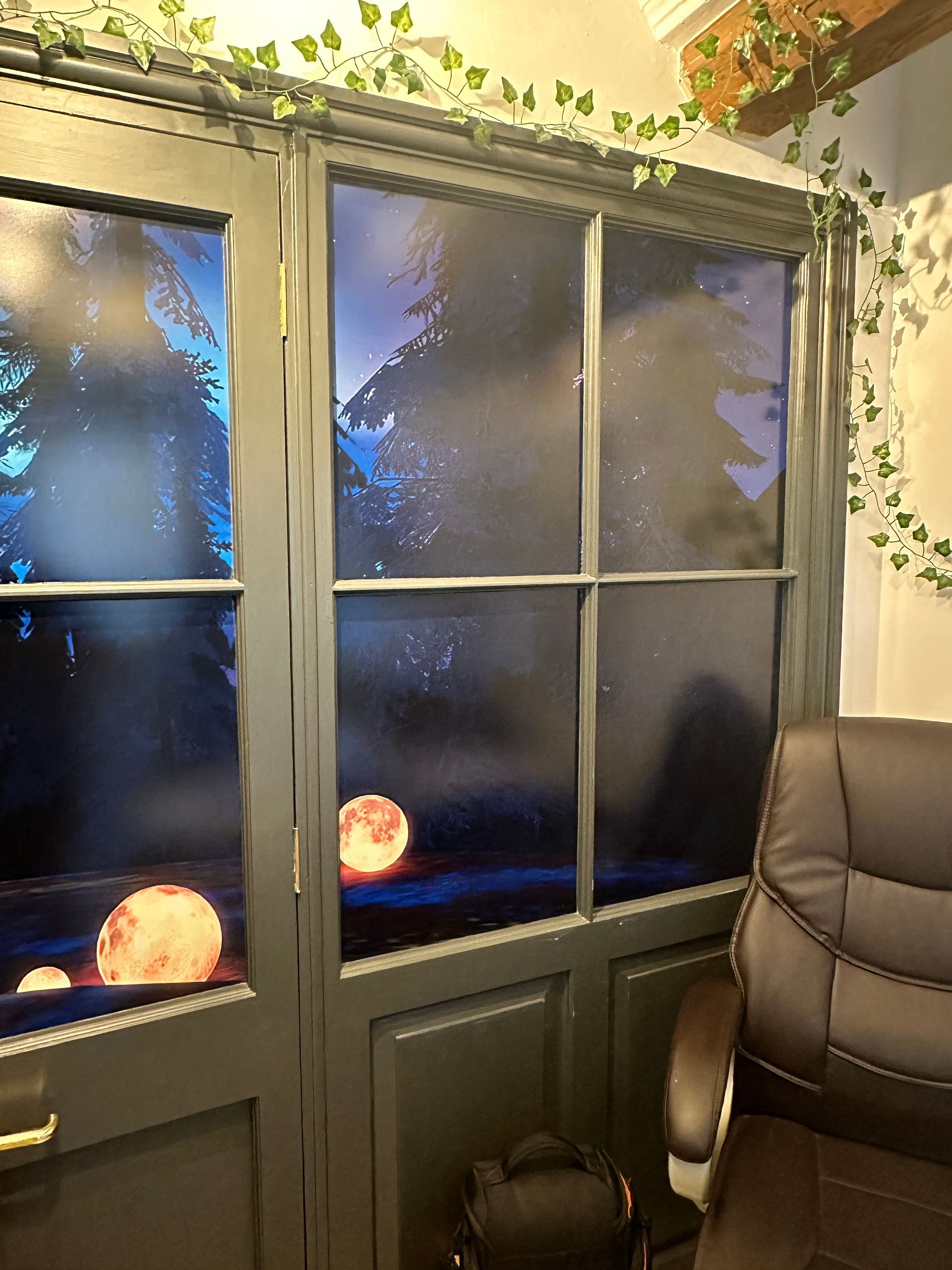 A room with a chair and a window with a picture of the moon on it.