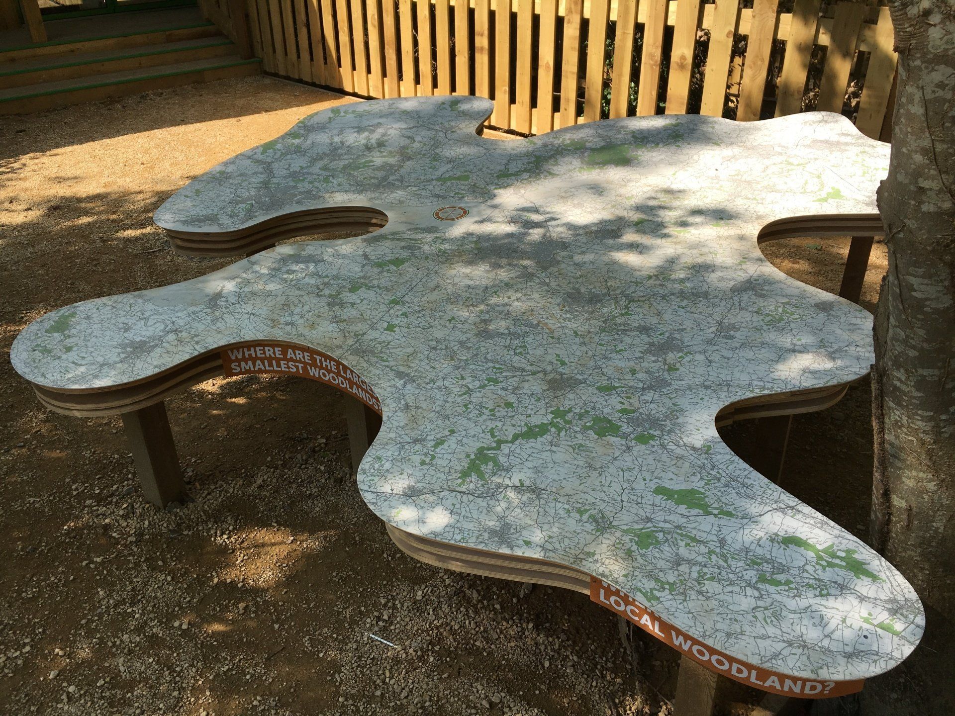 A wooden table with a map on it is sitting under a tree.