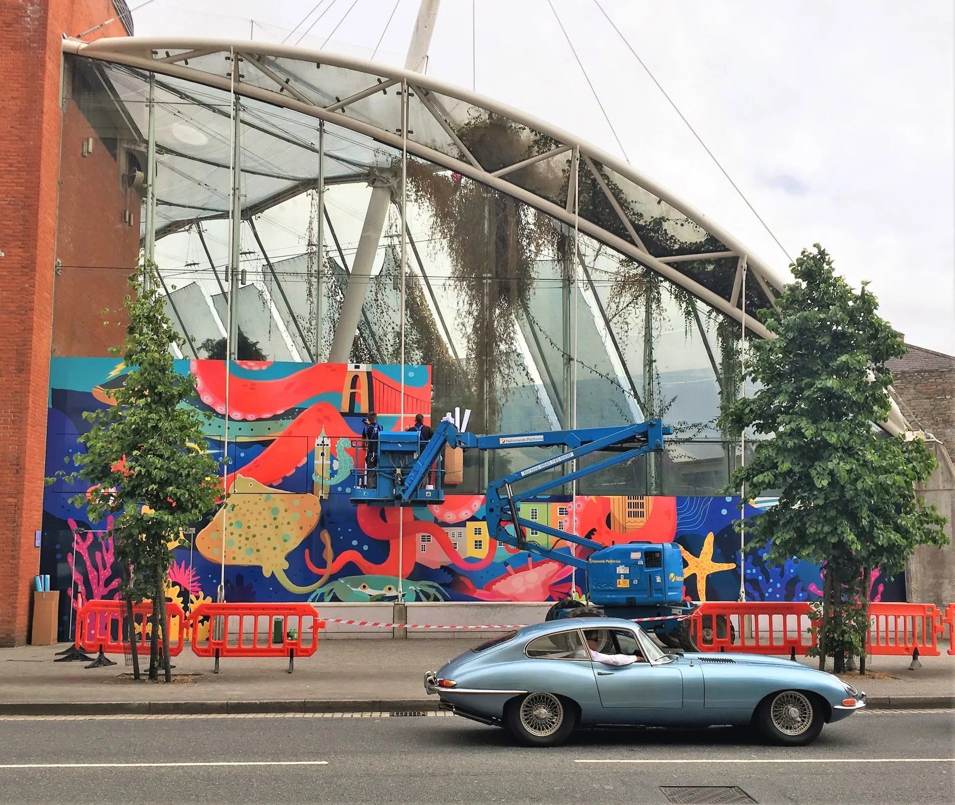 A blue car is parked in front of a building with a mural on it