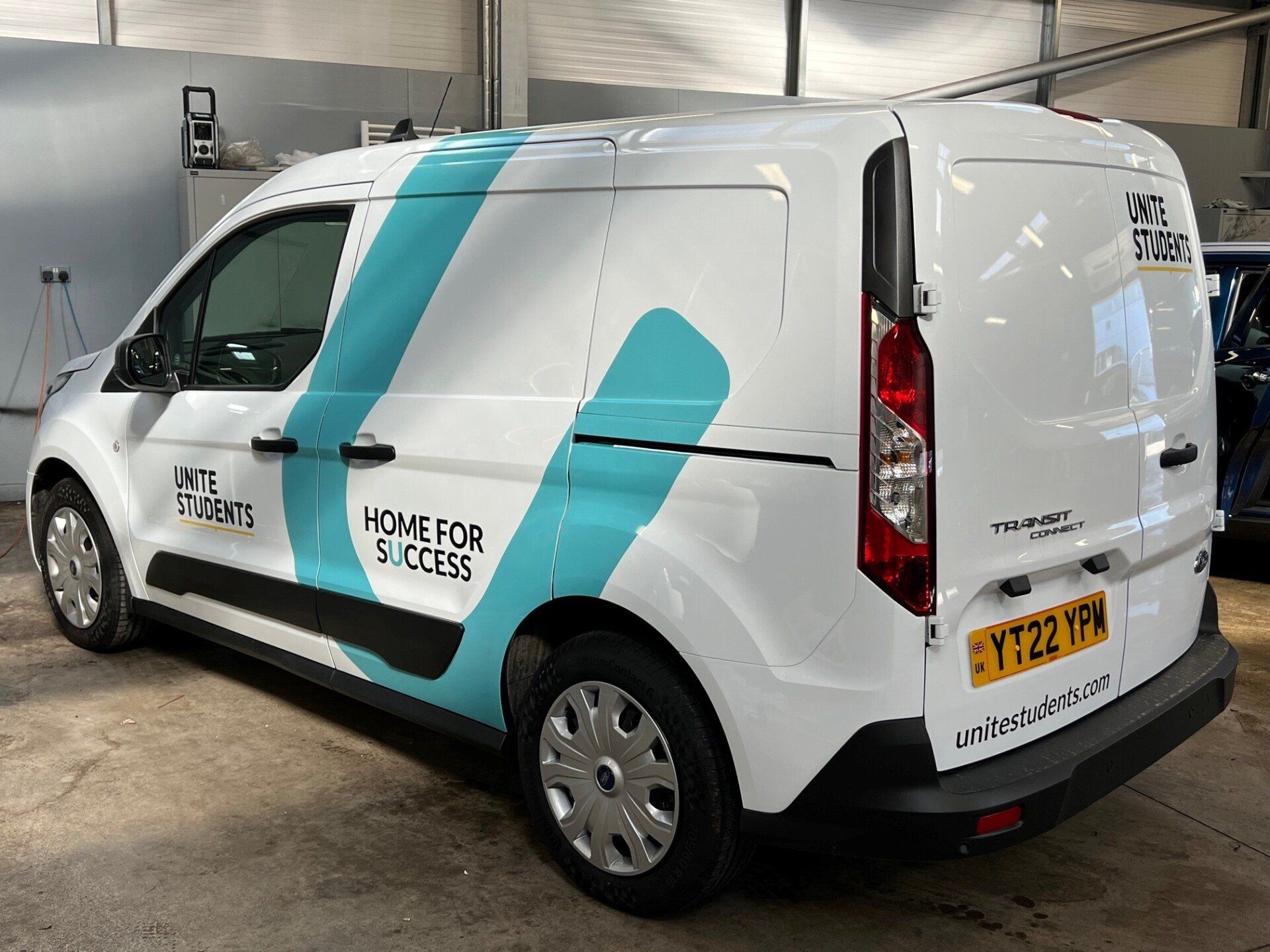A white van with blue stripes on the side is parked in a garage.