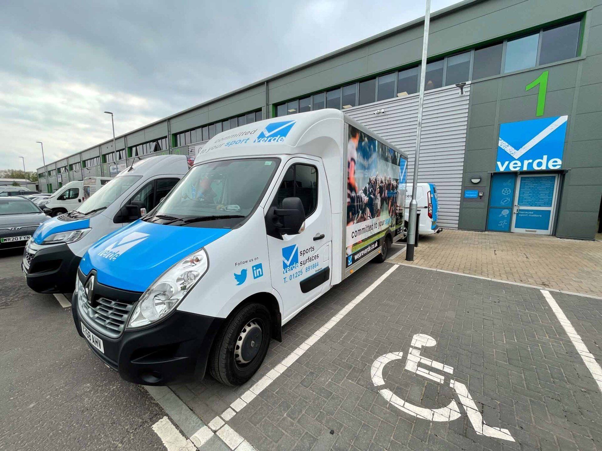 Three vans are parked in a handicapped parking spot in front of a building.