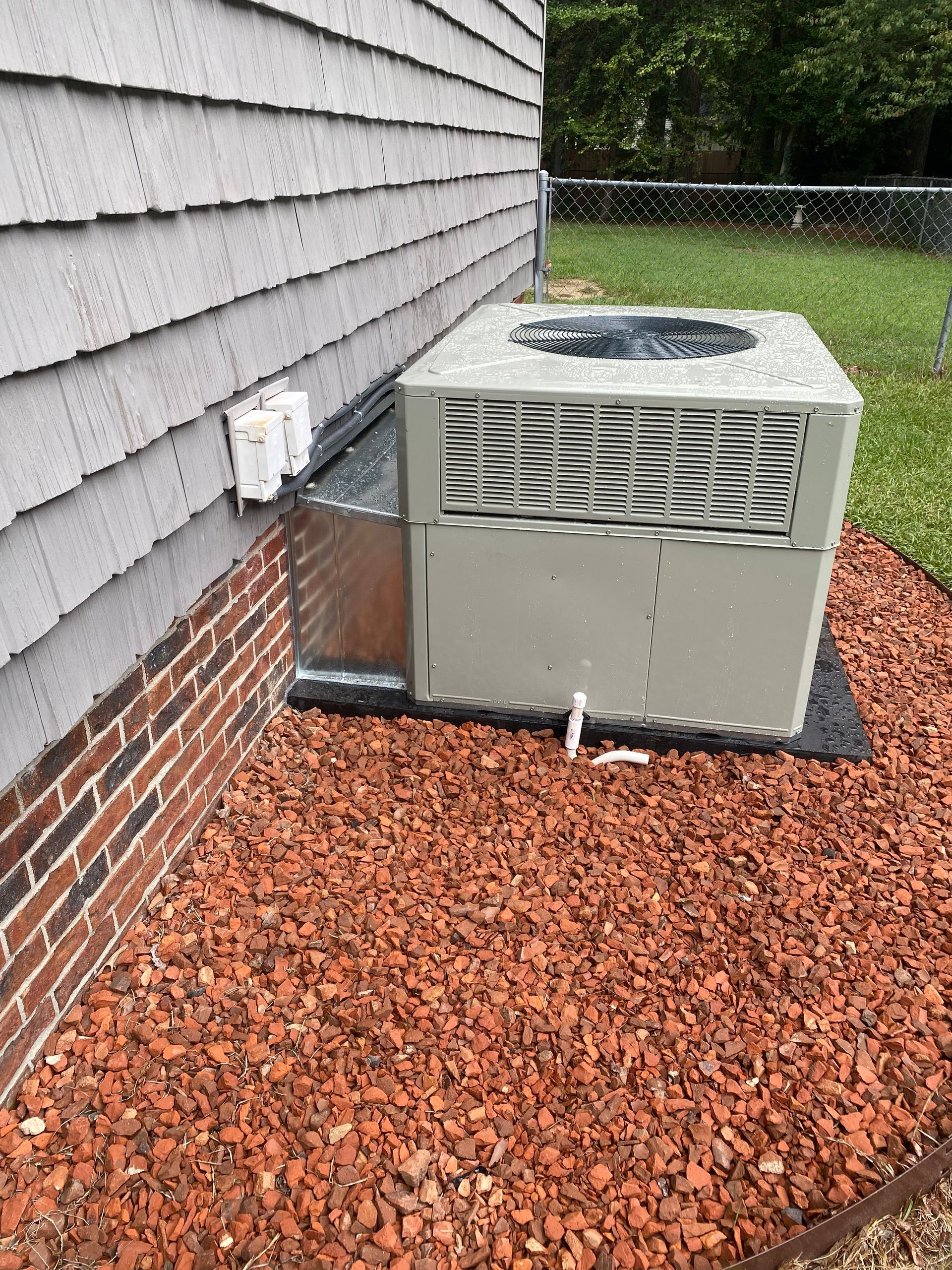 an air conditioner is sitting on top of a pile of gravel next to a brick building .