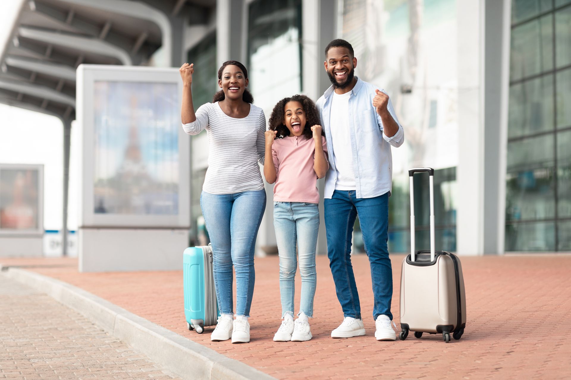 Family of three with suitcases celebrate travel success at an airport, smiling with raised fists