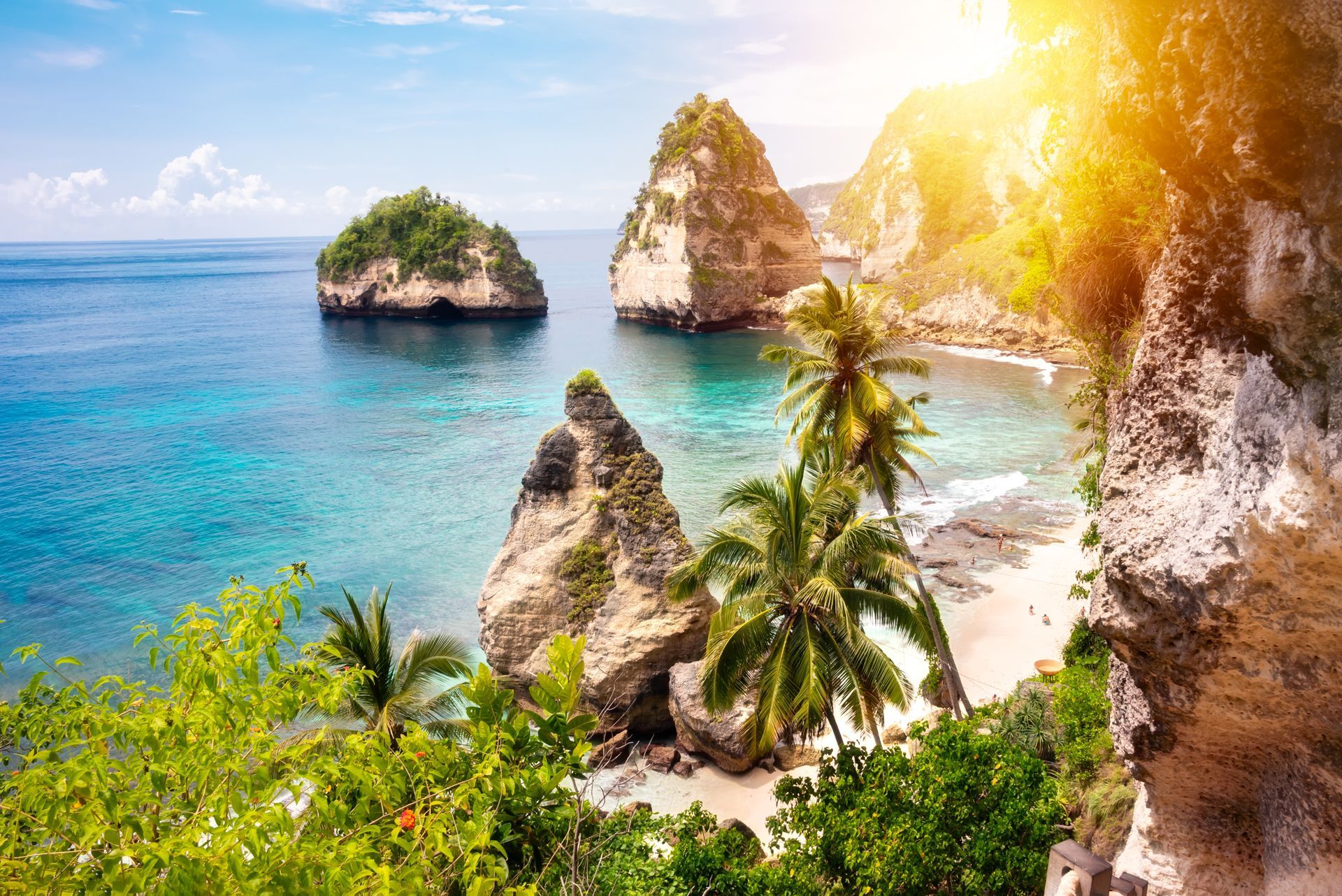 Tropical beach with turquoise water, rocky islands, palm trees, and sunlit cliffs
