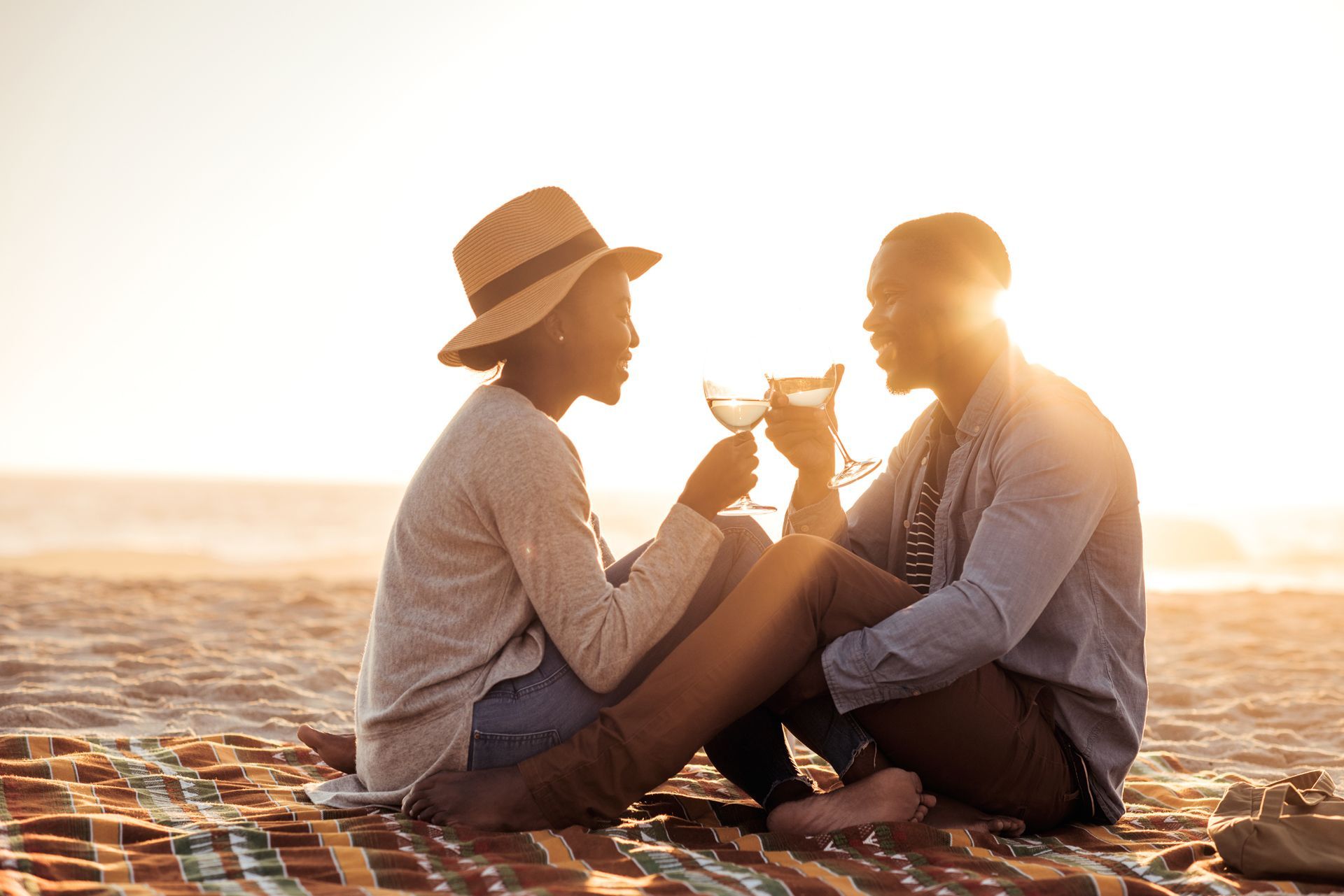 Couple toasting drinks on beach blanket at sunset