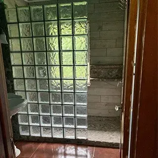 A bathroom with a walk in shower and a glass block wall.
