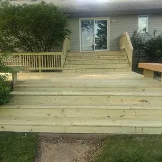A wooden deck with stairs and a bench in front of a house.