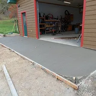 A concrete walkway is being built in front of a garage.