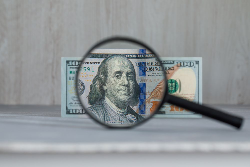 A $100 bill viewed through a magnifying glass, showing Benjamin Franklin's face.