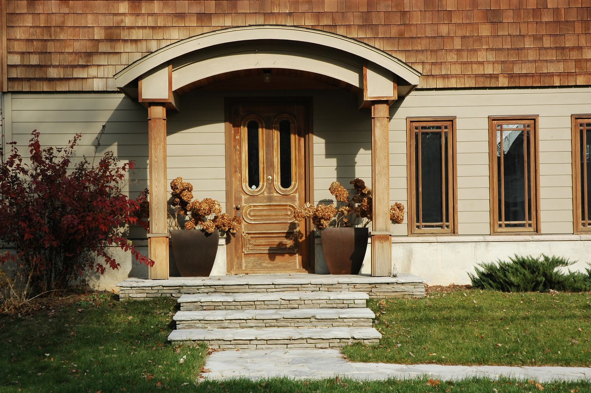 House entrance with arched wooden porch, stone steps, and potted plants.