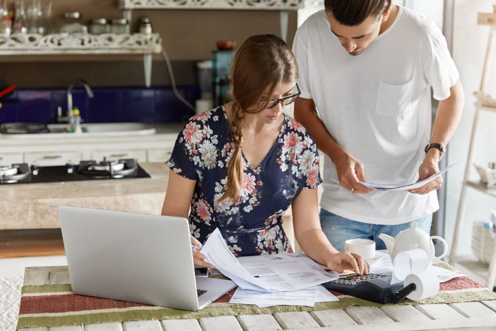 Couple reviewing financial documents with a laptop and calculator in a kitchen.