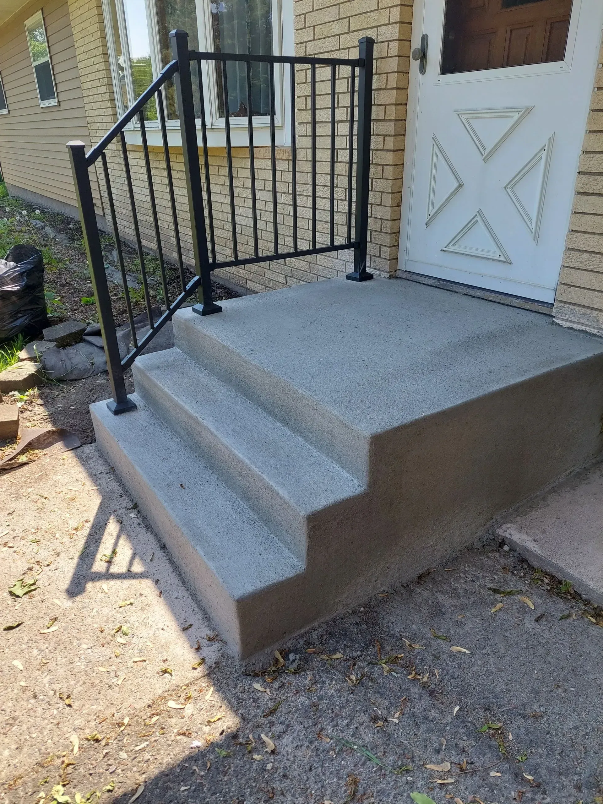 A concrete porch with stairs and a wrought iron railing.