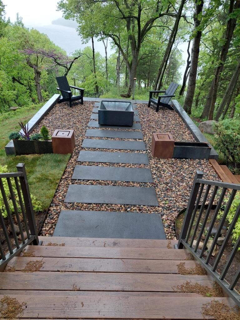 A wooden walkway leading to a patio with a fire pit and chairs.