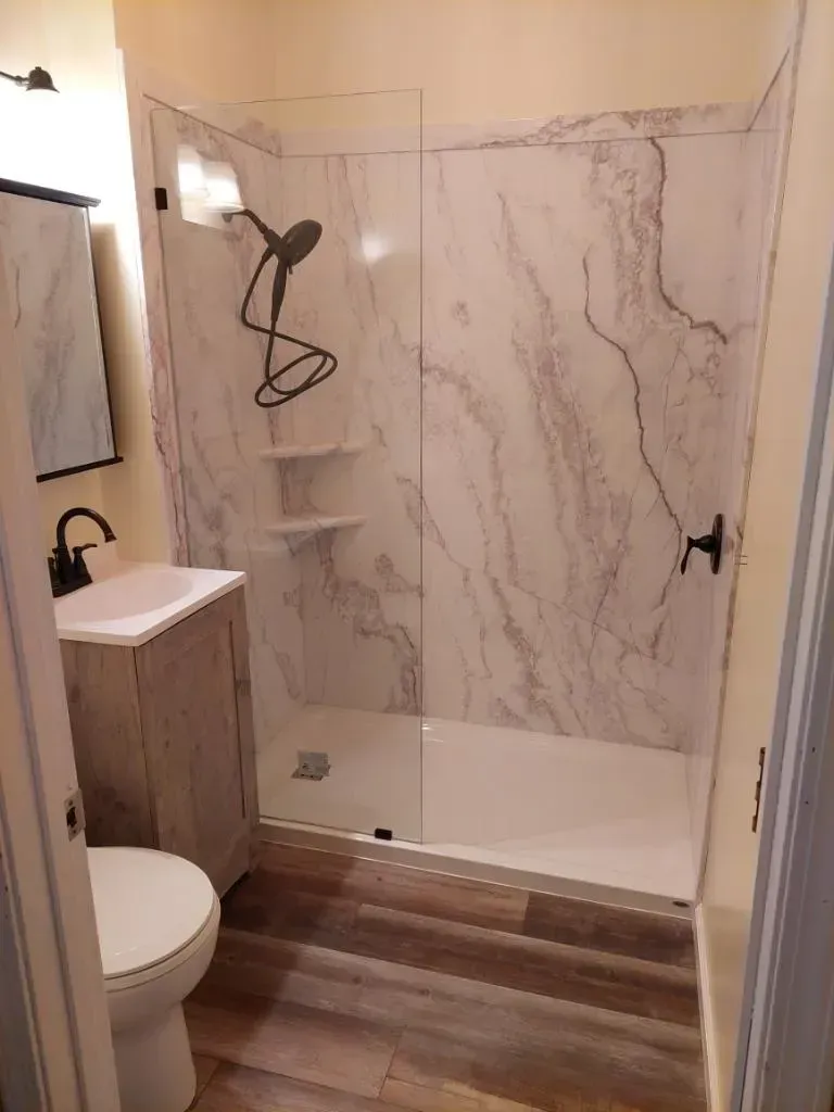 A bathroom with a walk in shower , toilet , sink and mirror.