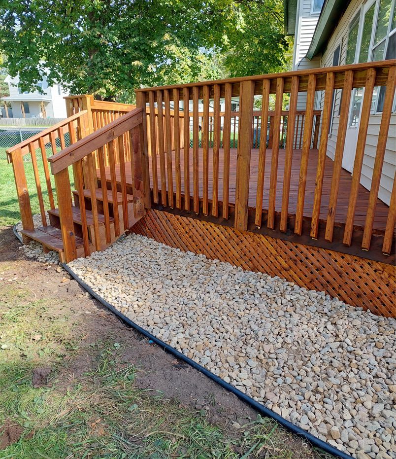 A wooden deck with stairs and gravel in front of a house.
