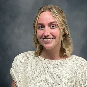 Smiling person in a cream knit sweater against a gray studio backdrop