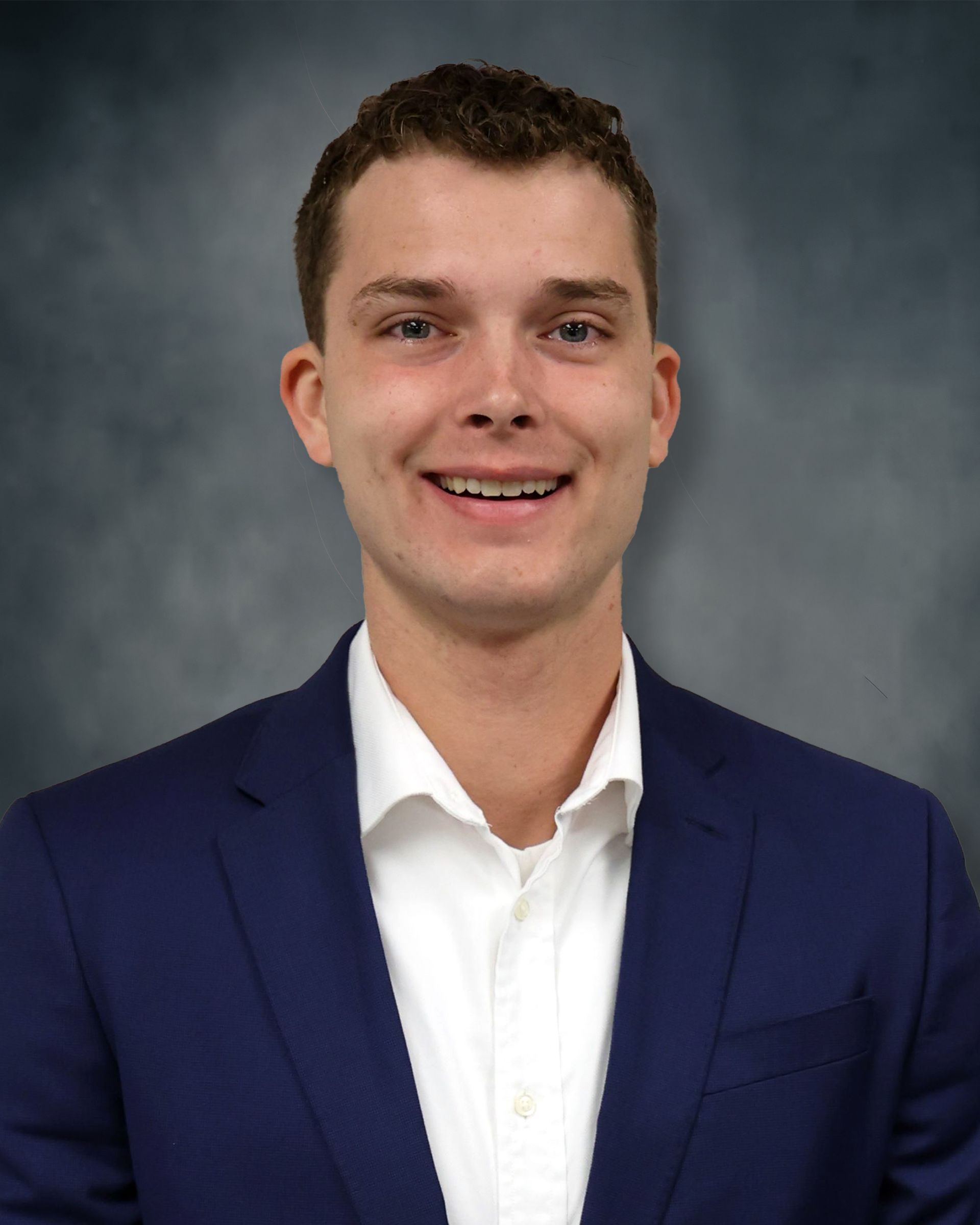 Portrait of a smiling person in a blue blazer and white shirt against a gray studio backdrop