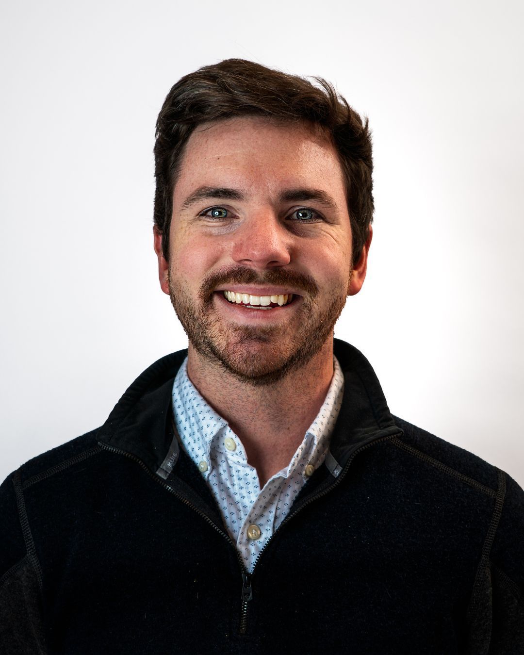 Smiling man in a patterned white shirt against a gray studio backdrop