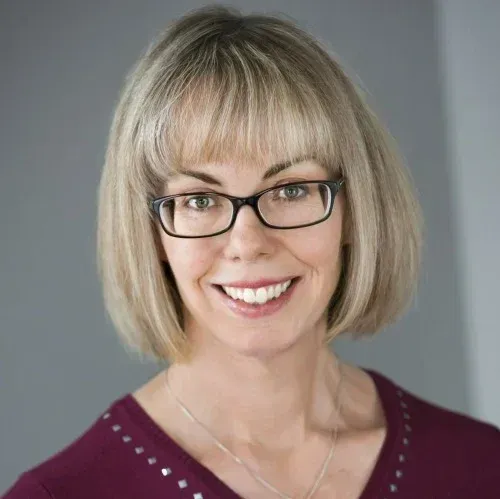 A woman wearing glasses and a red shirt is smiling for the camera.